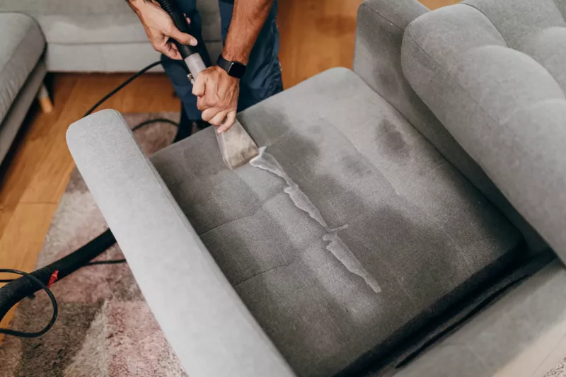 Handsome zoung man cleaning furniture. Process of deep furniture cleaning, removing dirt from sofa. Washing concept.